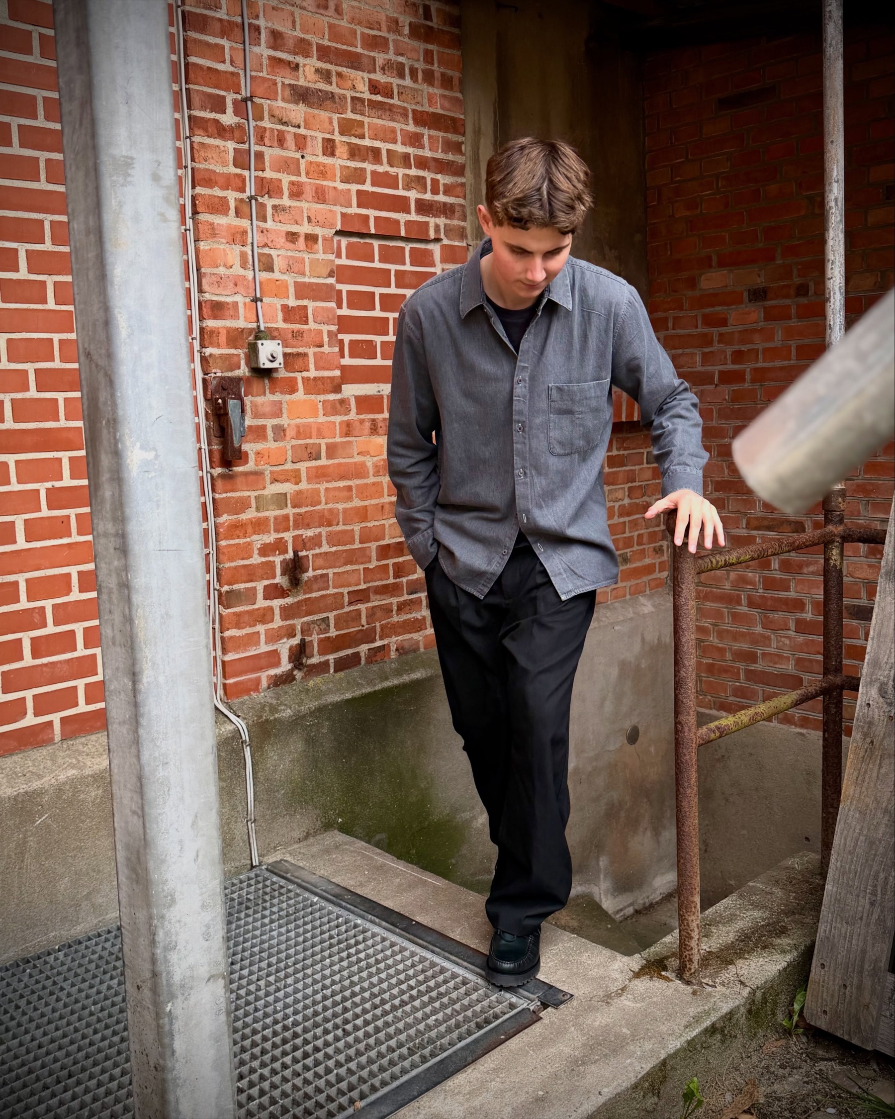Ung mand i grå overshirt på en ståltrappe ved en rød murstensmur